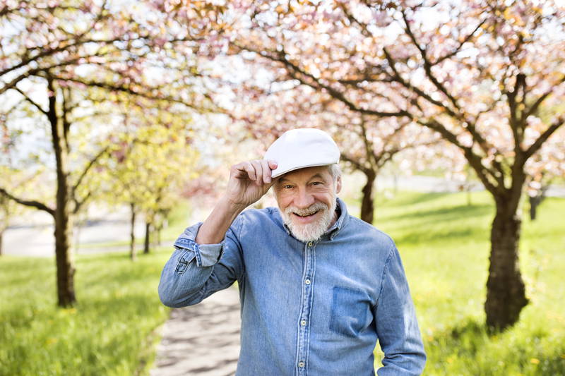 older man in blue shirt and shite hat outside smiling